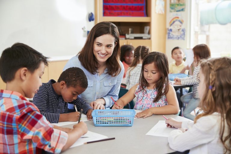 Teacher sitting at table with young school kids in classroom